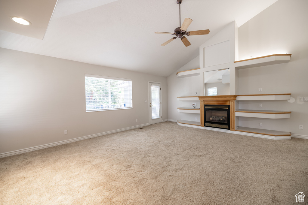 Unfurnished living room with ceiling fan, carpet flooring, high vaulted ceiling, and a glass covered fireplace