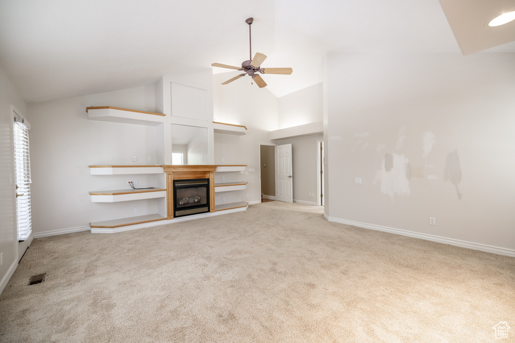 Unfurnished living room with ceiling fan, carpet, high vaulted ceiling, and a glass covered fireplace