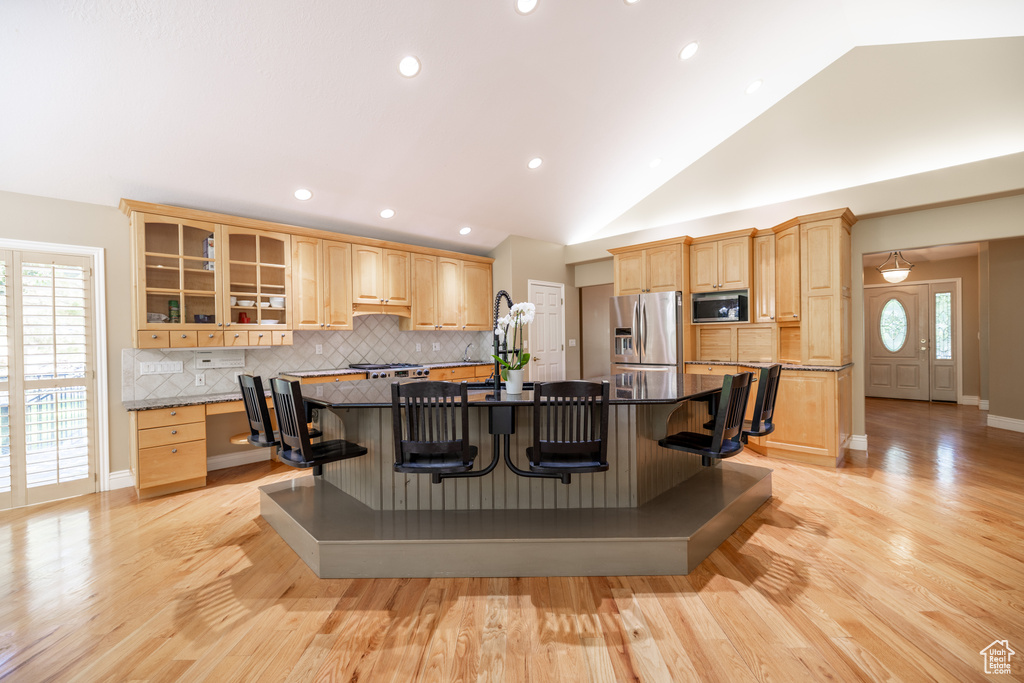 Kitchen with stainless steel appliances, a kitchen breakfast bar, light brown cabinetry, tasteful backsplash, and an island with sink