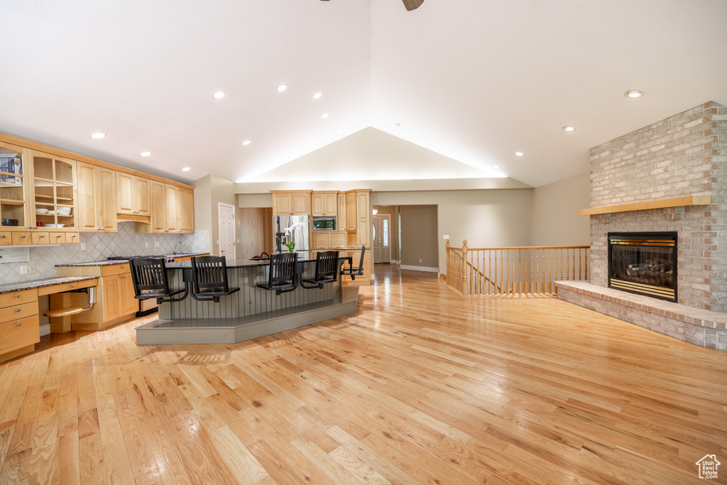 Living room featuring light wood-type flooring, lofted ceiling, a brick fireplace, and recessed lighting