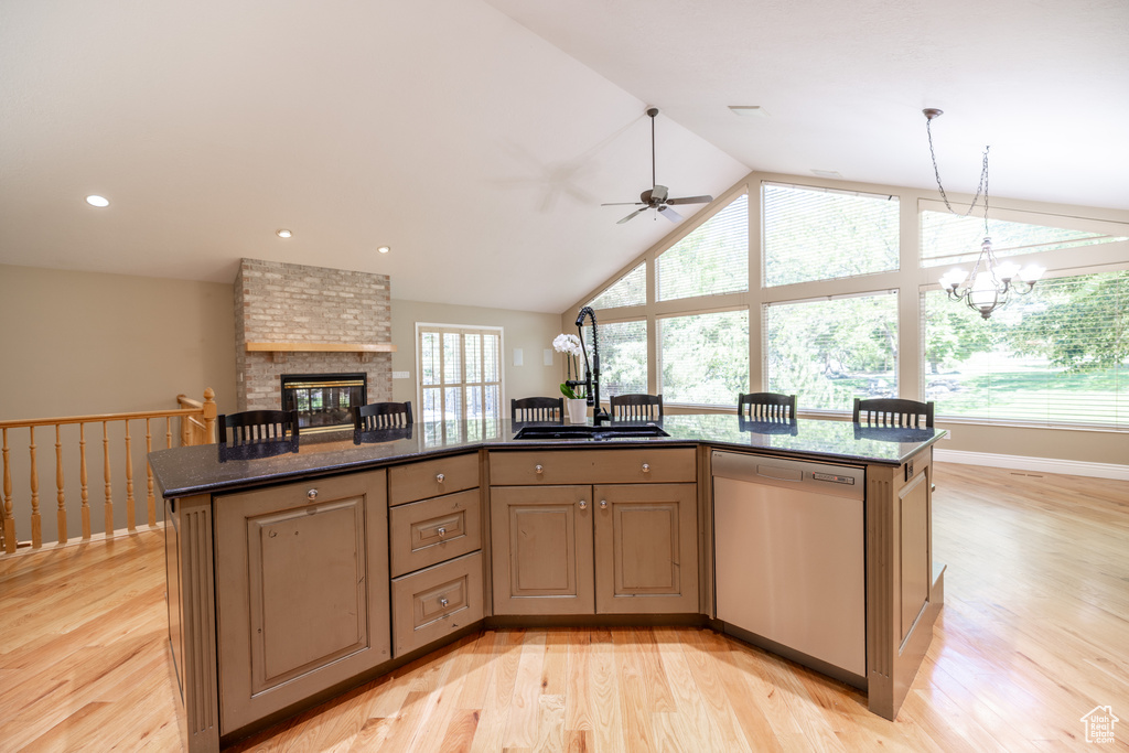 Kitchen featuring dishwasher, light wood-type flooring, vaulted ceiling, ceiling fan, and a brick fireplace