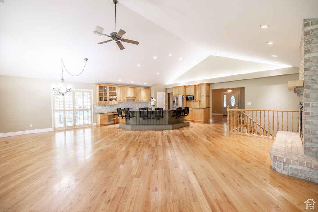 Living room with a ceiling fan, vaulted ceiling, light wood-style floors, a chandelier, and recessed lighting