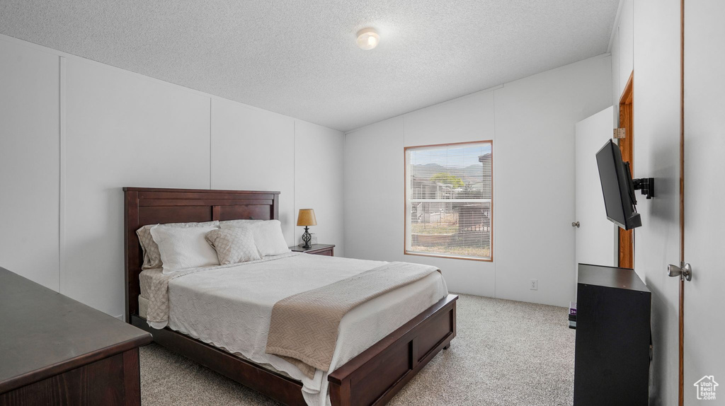 Bedroom featuring vaulted ceiling, light carpet, and a textured ceiling