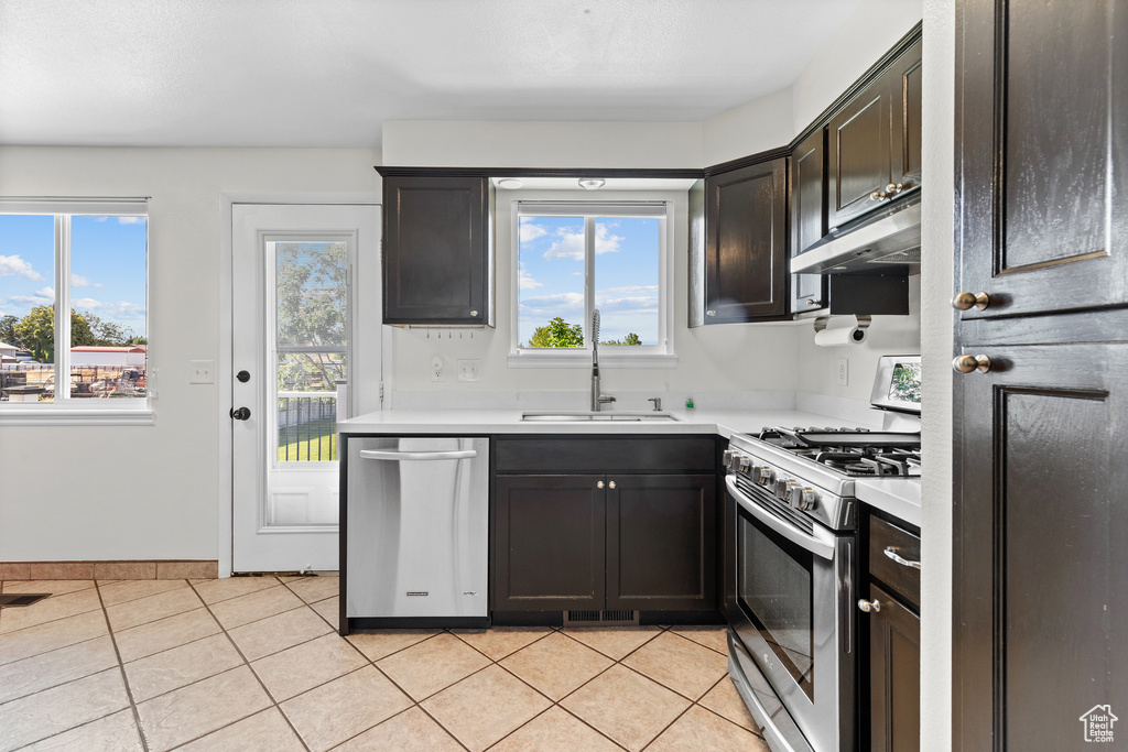Kitchen with stainless steel appliances, under cabinet range hood, light countertops, light tile patterned floors, and plenty of natural light