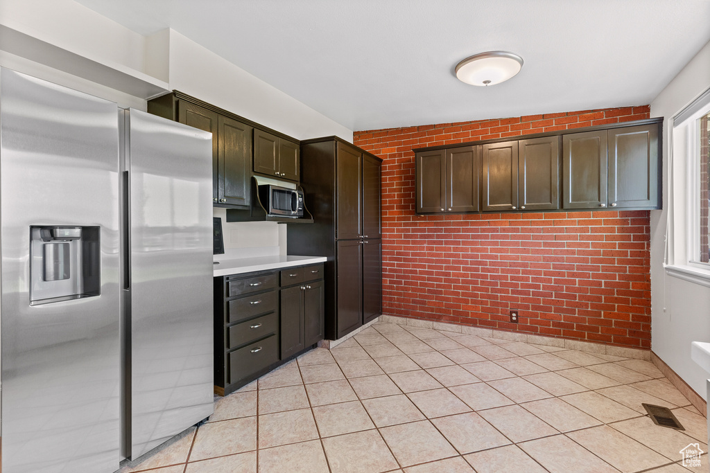 Kitchen featuring stainless steel appliances, brick wall, light tile patterned floors, light countertops, and dark brown cabinetry