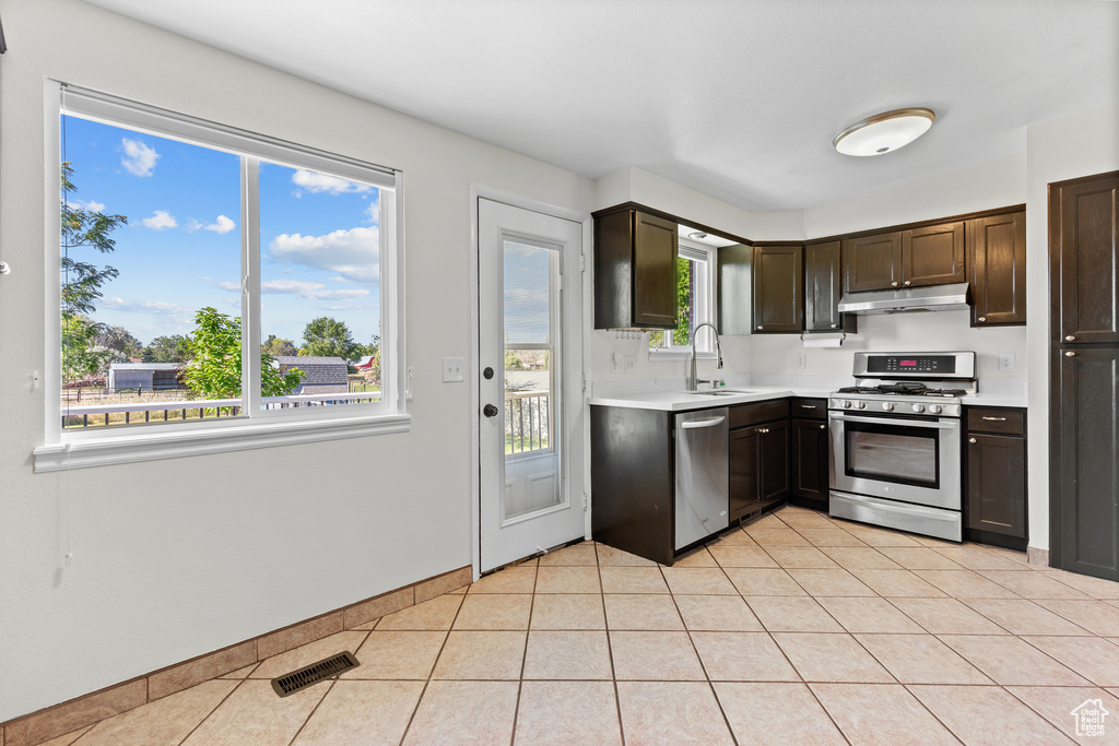 Kitchen featuring stainless steel appliances, under cabinet range hood, light countertops, dark brown cabinetry, and light tile patterned floors