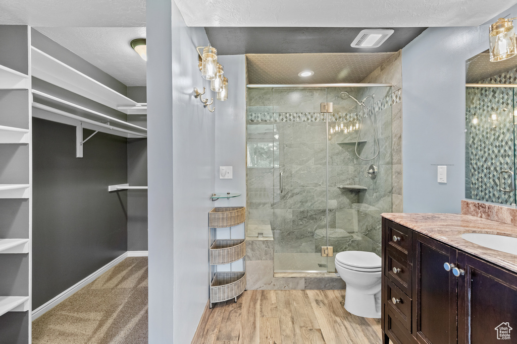 Bathroom featuring a walk in closet, vanity, a stall shower, and wood finished floors