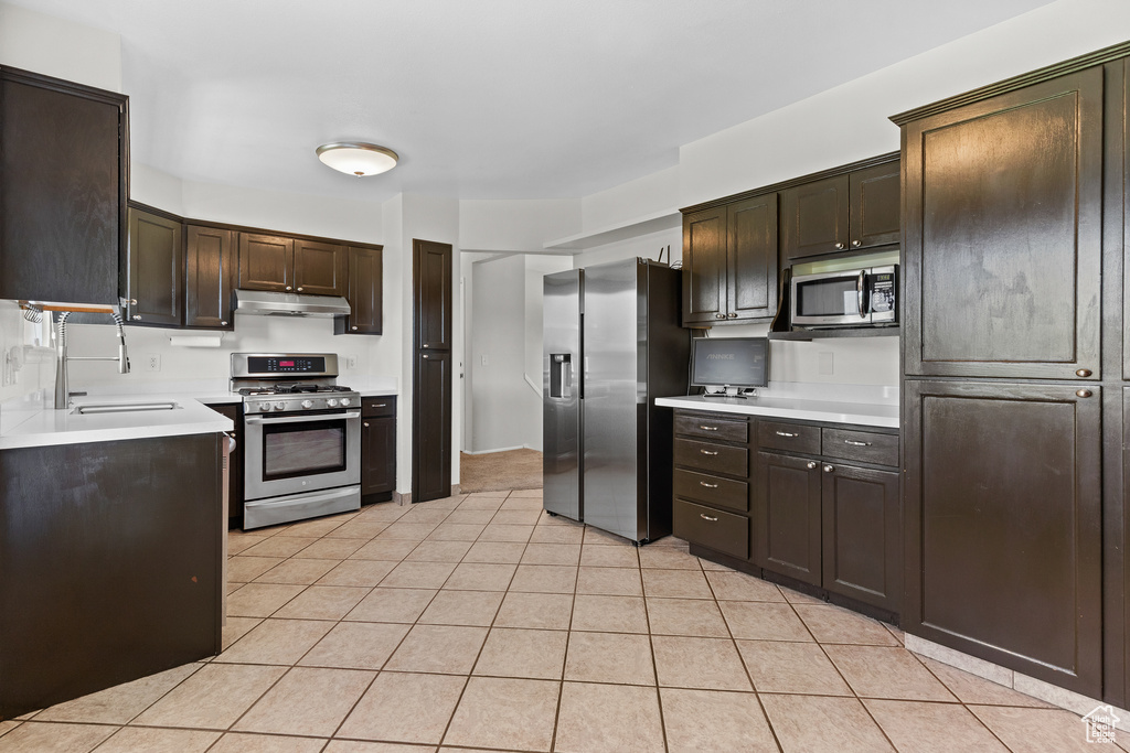 Kitchen featuring stainless steel appliances, under cabinet range hood, dark brown cabinetry, light countertops, and light tile patterned floors