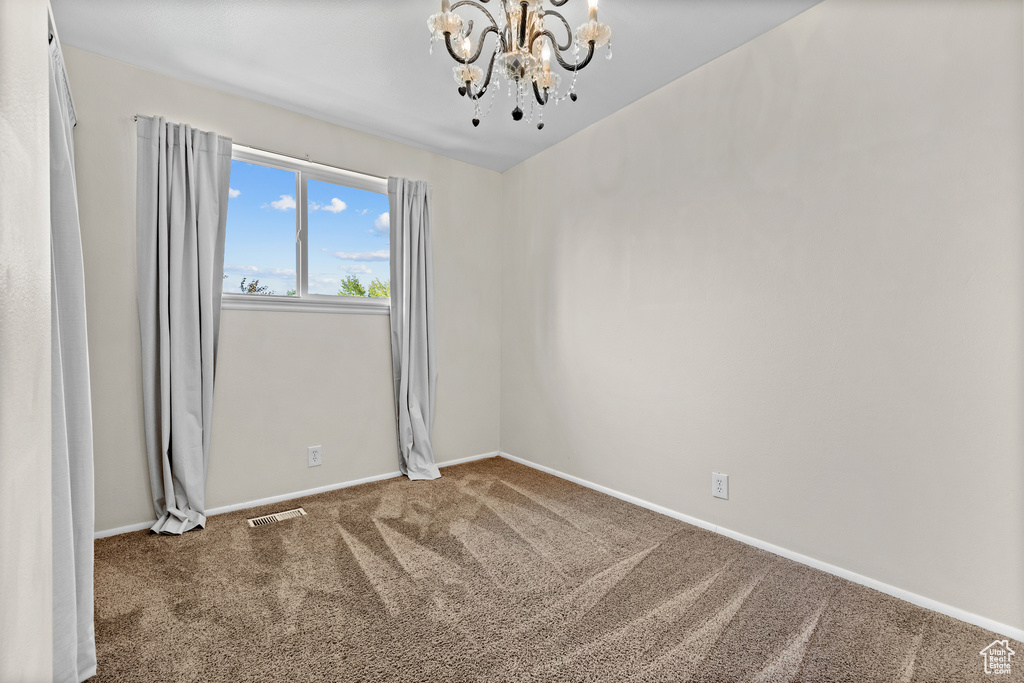 Carpeted spare room with a chandelier and baseboards