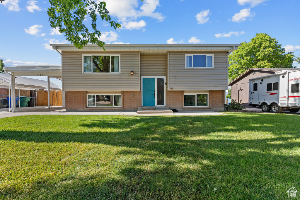 Bi-level home featuring brick siding, entry steps, a carport, and a front yard