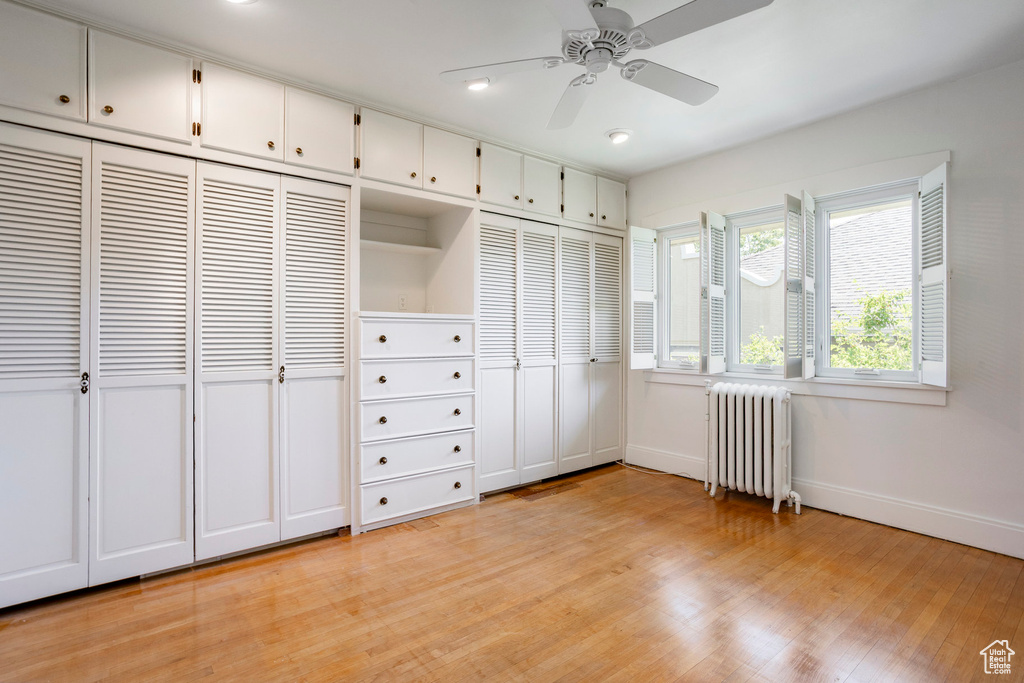 Unfurnished bedroom with radiator heating unit, light wood finished floors, and two closets
