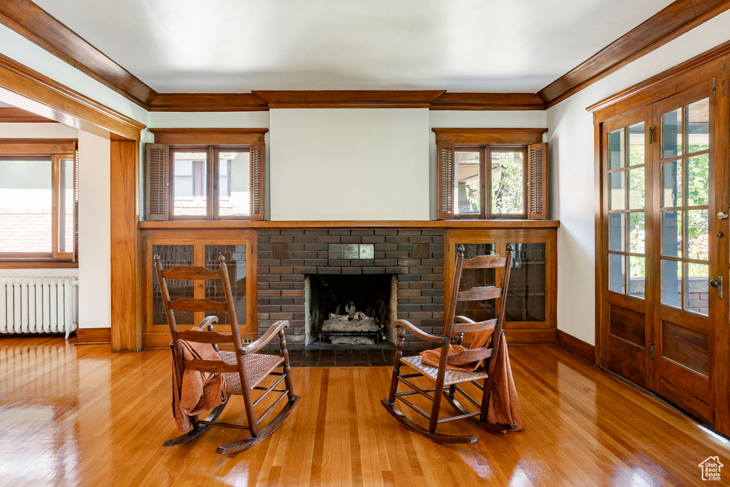 Living area featuring radiator, wood finished floors, a fireplace, ornamental molding, and french doors