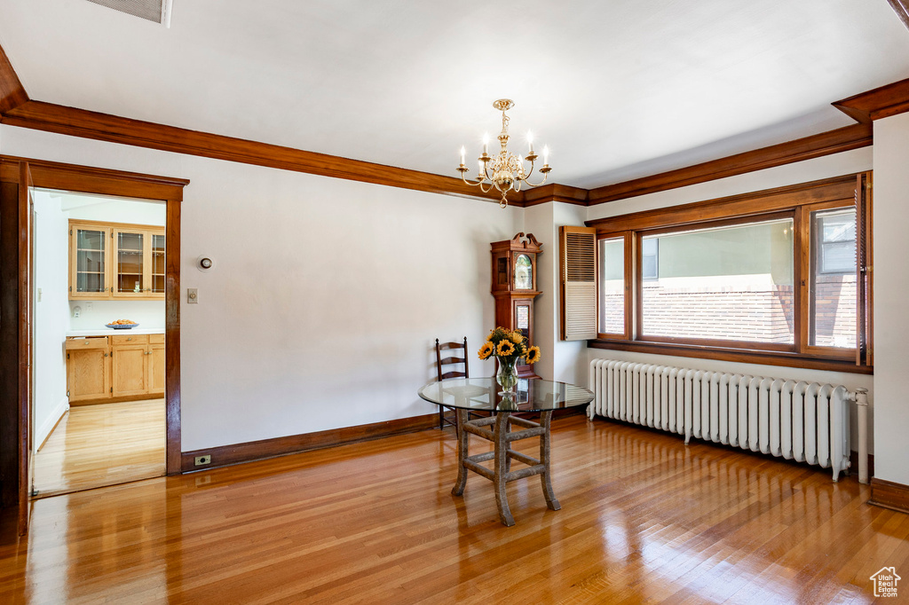 Dining room featuring radiator, a chandelier, light wood finished floors, and crown molding