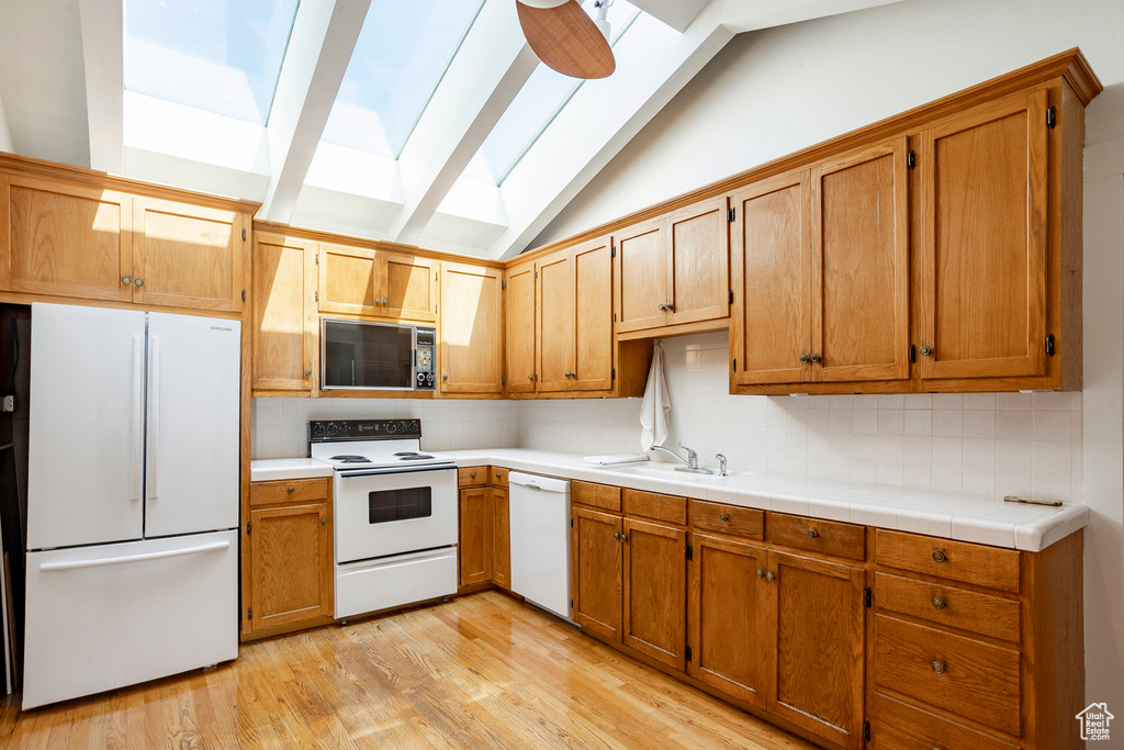 Kitchen with white appliances, a skylight, backsplash, light wood-type flooring, and light countertops