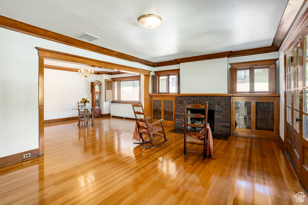 Living area featuring radiator heating unit, a fireplace, a chandelier, wood finished floors, and crown molding