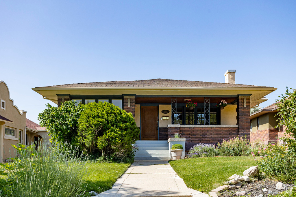 View of front of home featuring brick siding, a porch, a front lawn, and a chimney