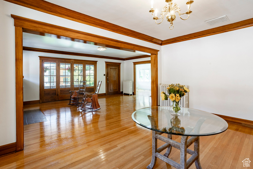 Dining room featuring radiator heating unit, light wood-style flooring, a chandelier, ornamental molding, and plenty of natural light