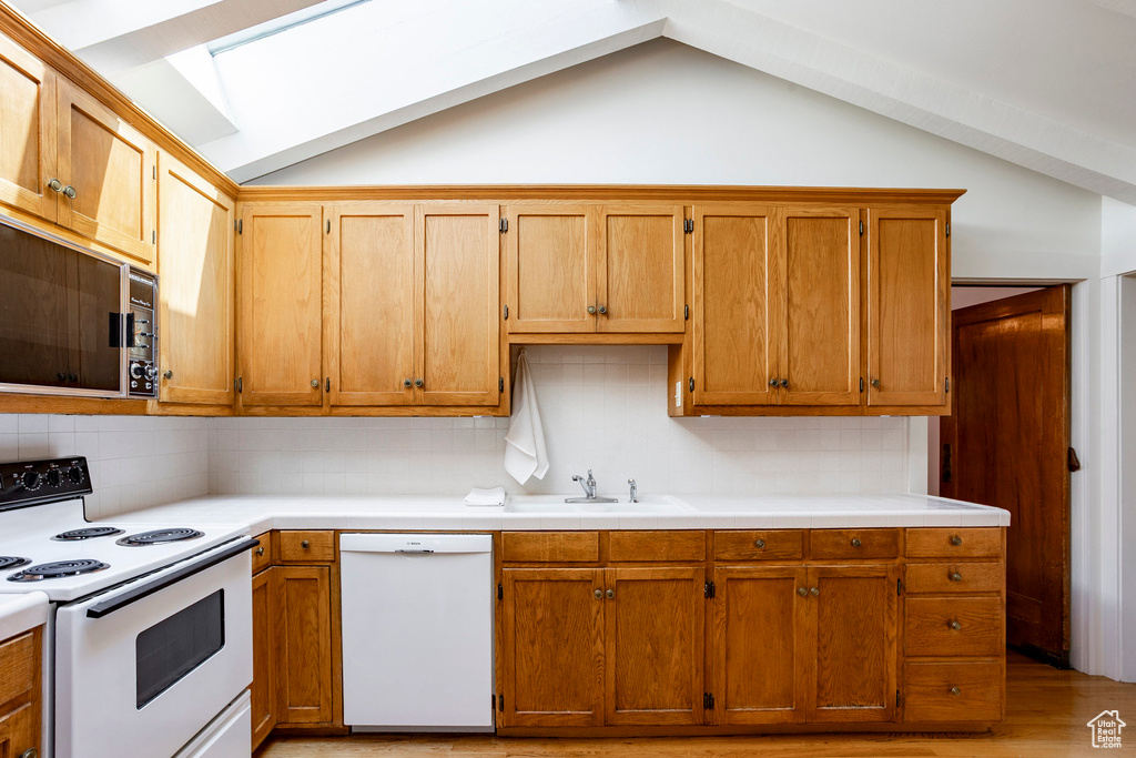 Kitchen with white appliances, lofted ceiling, tasteful backsplash, and light countertops