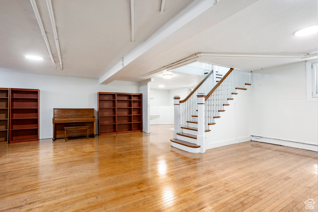 Basement with light wood finished floors, stairway, and a baseboard heating unit