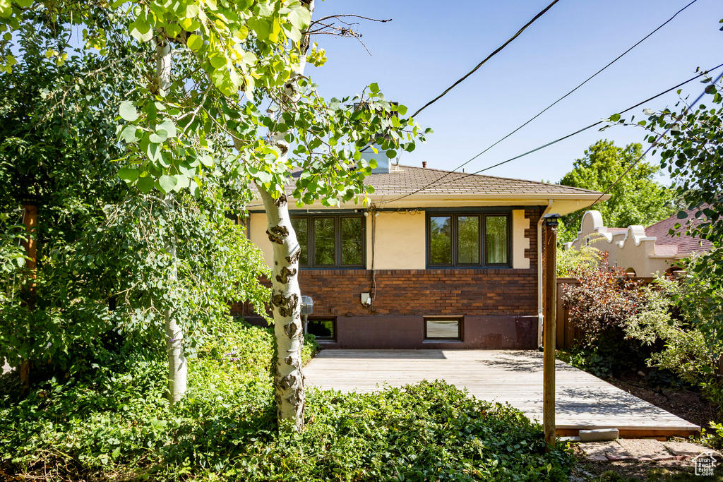 Back of property with a deck, brick siding, and roof with shingles