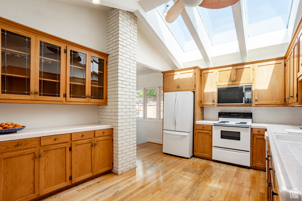 Kitchen featuring white appliances, a skylight, tile countertops, light wood finished floors, and tasteful backsplash