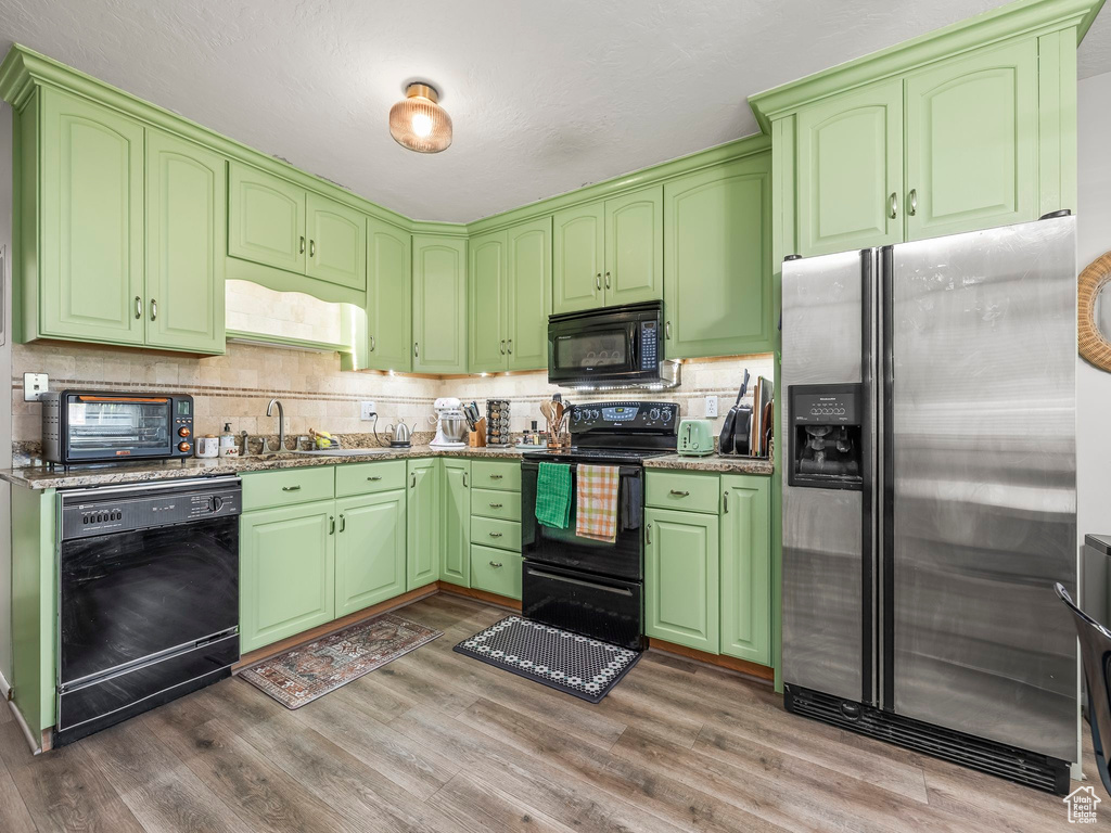 Kitchen featuring black appliances, wood finished floors, tasteful backsplash, and stone countertops