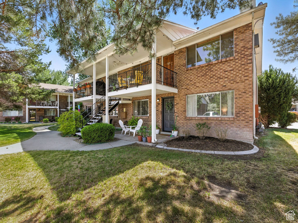 View of front facade with brick siding, a front yard, a balcony, and stairway