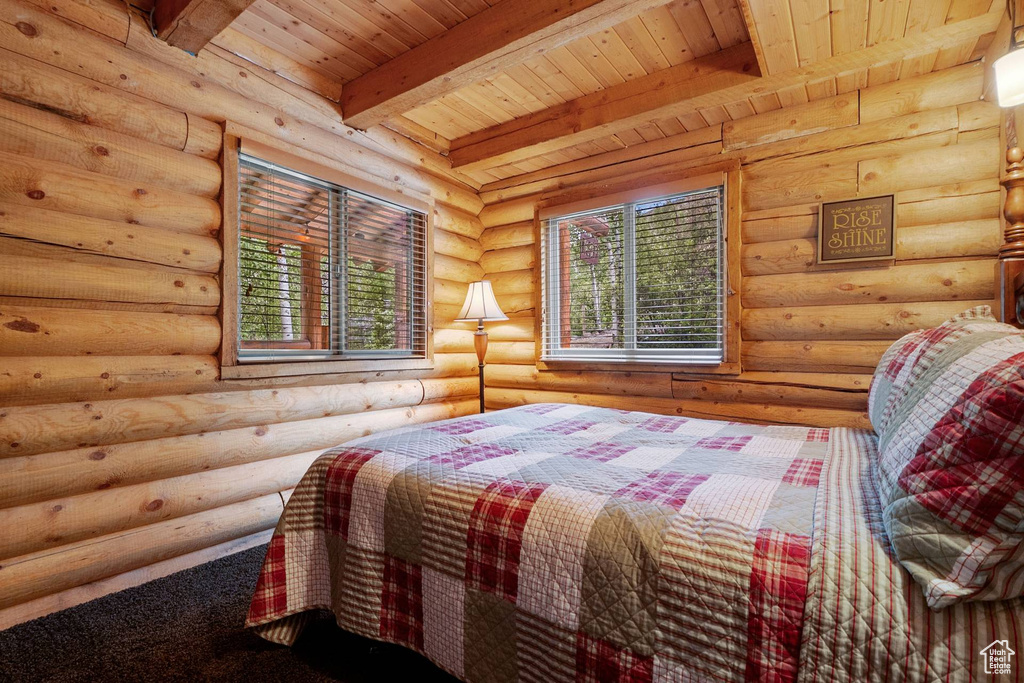 Bedroom with a wooden ceiling with exposed beams and log walls