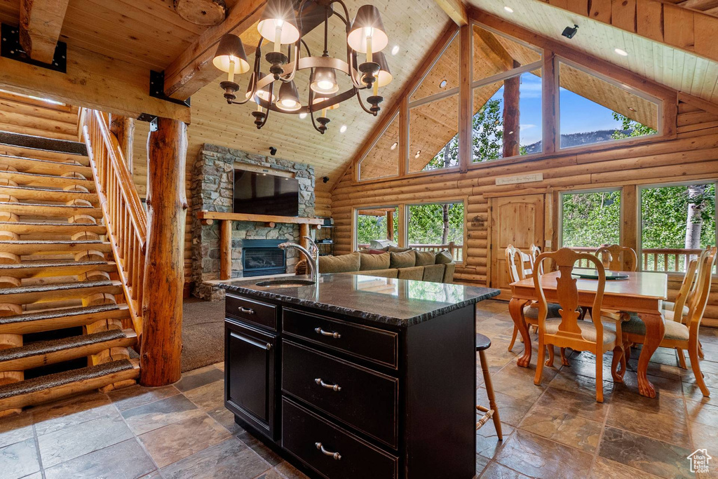 Kitchen with rustic walls, high vaulted ceiling, dark cabinets, a fireplace, and a wooden ceiling with exposed beams