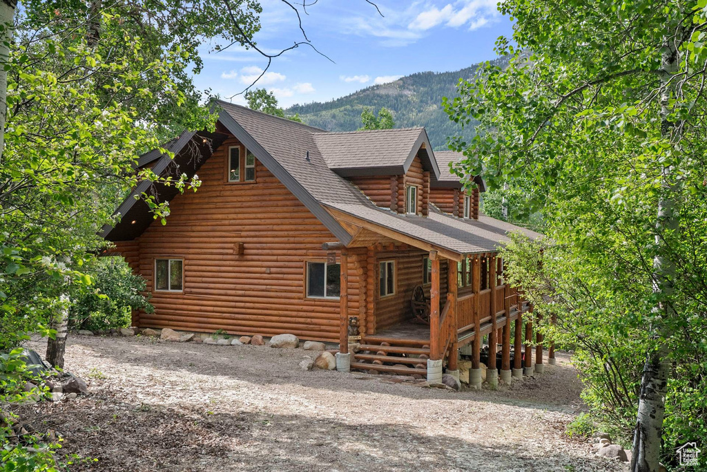 Back of house with log exterior, a porch, a mountain view, a shingled roof, and dirt driveway
