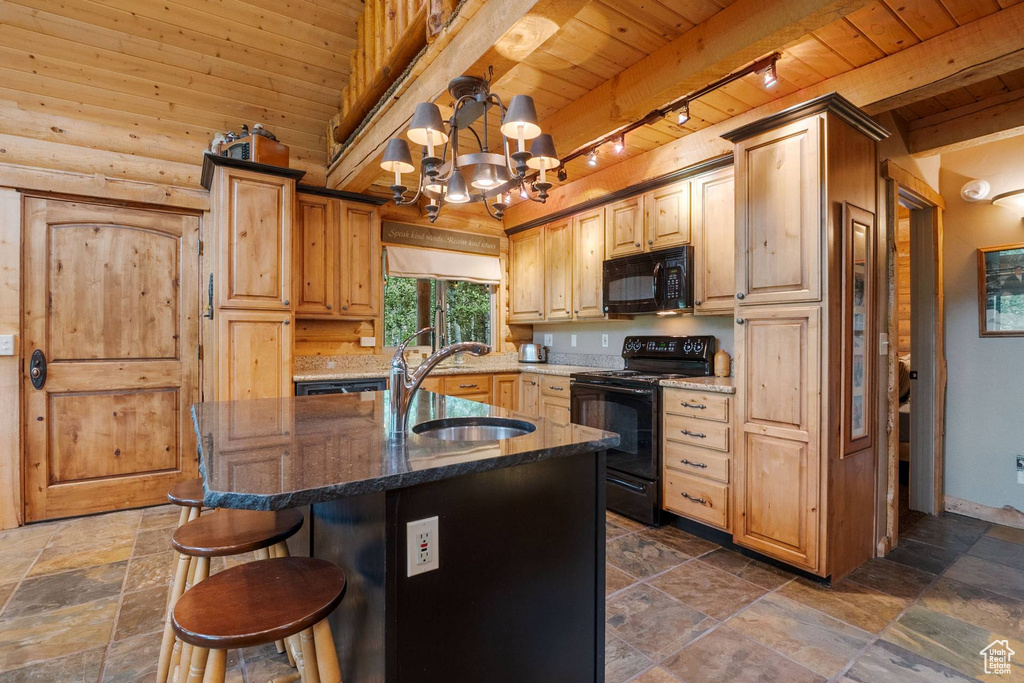 Kitchen with a wood ceiling with exposed beams, black appliances, rail lighting, stone tile floors, and dark stone countertops