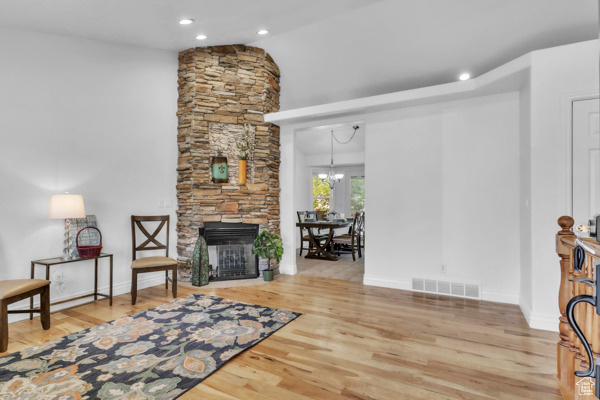 Living room featuring wood finished floors, a stone fireplace, recessed lighting, a chandelier, and lofted ceiling