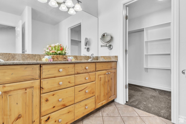 Full bath with double vanity, tile patterned floors, and a spacious closet