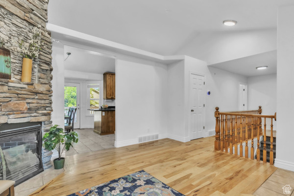 Living room featuring light wood finished floors, a stone fireplace, and vaulted ceiling