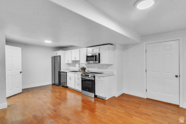 Kitchen with appliances with stainless steel finishes, white cabinets, light wood finished floors, and light countertops