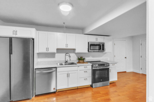 Kitchen with appliances with stainless steel finishes, light countertops, white cabinets, and light wood finished floors