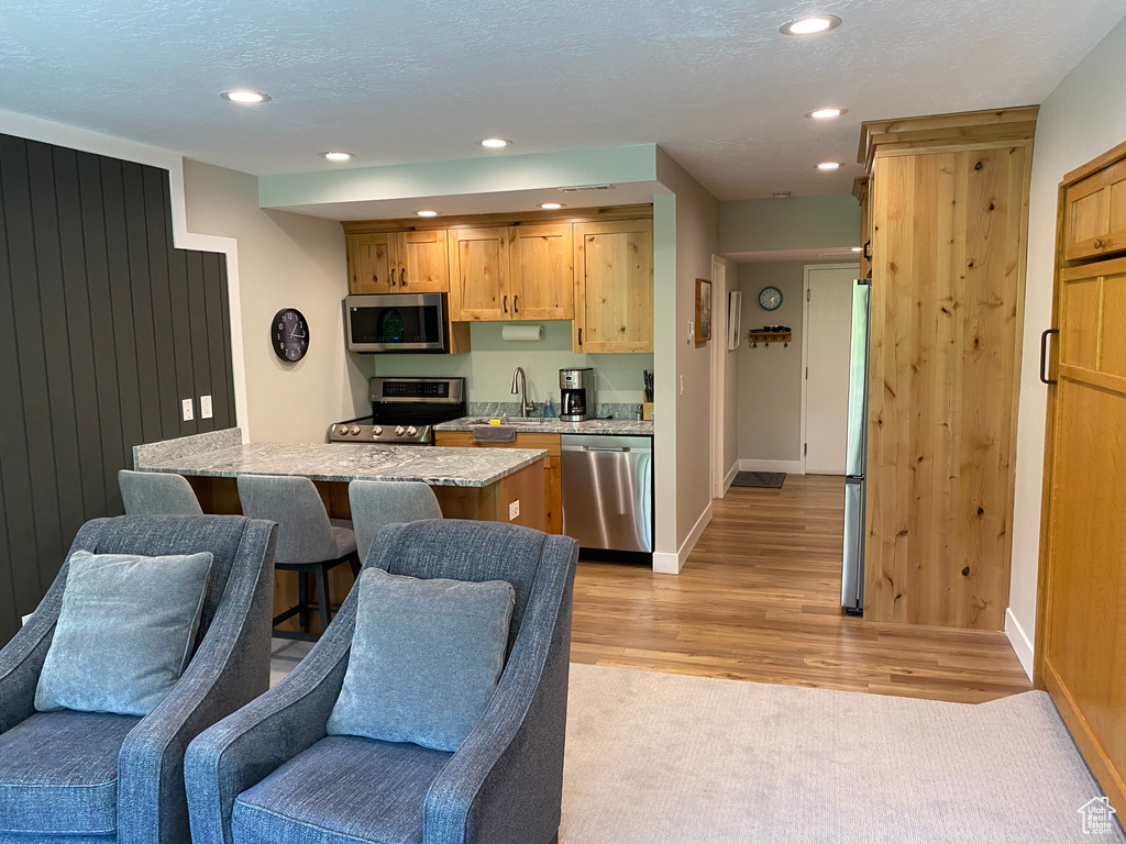 Kitchen with appliances with stainless steel finishes, light wood-style floors, open floor plan, recessed lighting, and light stone counters