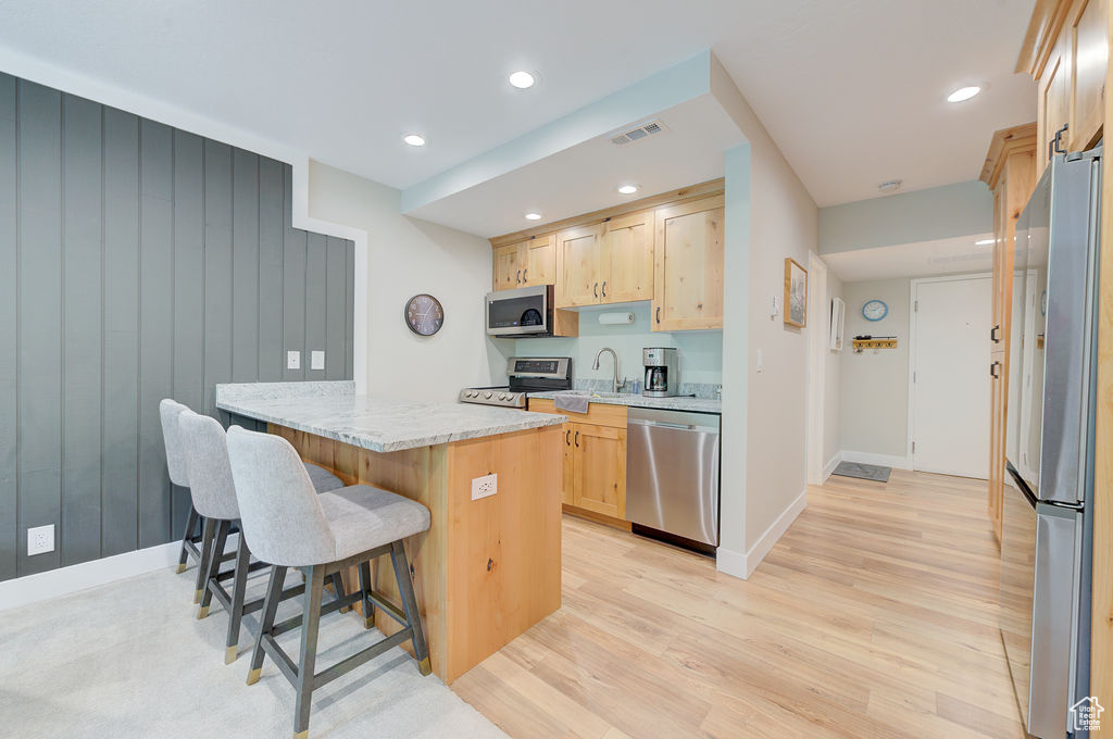 Kitchen with appliances with stainless steel finishes, light brown cabinets, a kitchen bar, light wood finished floors, and recessed lighting