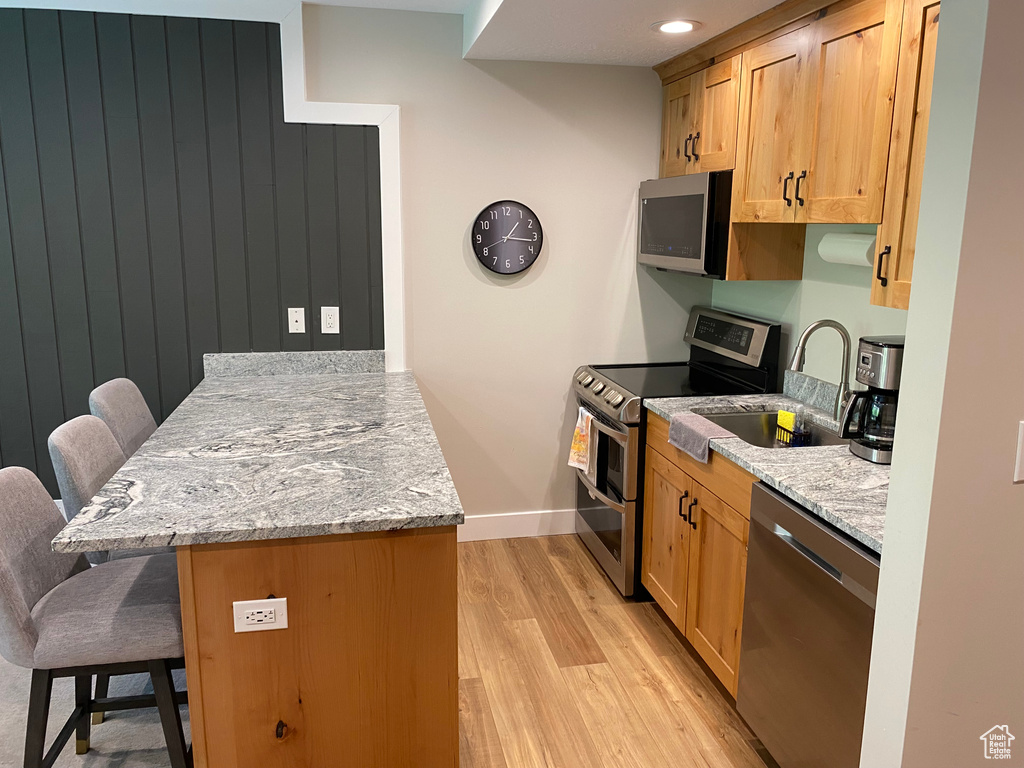 Kitchen featuring stainless steel appliances, a peninsula, a kitchen breakfast bar, light wood-type flooring, and light stone countertops