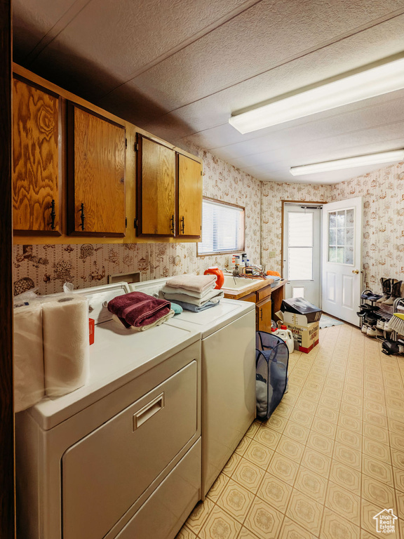 Laundry room featuring wallpapered walls, cabinet space, washing machine and clothes dryer, and a textured ceiling