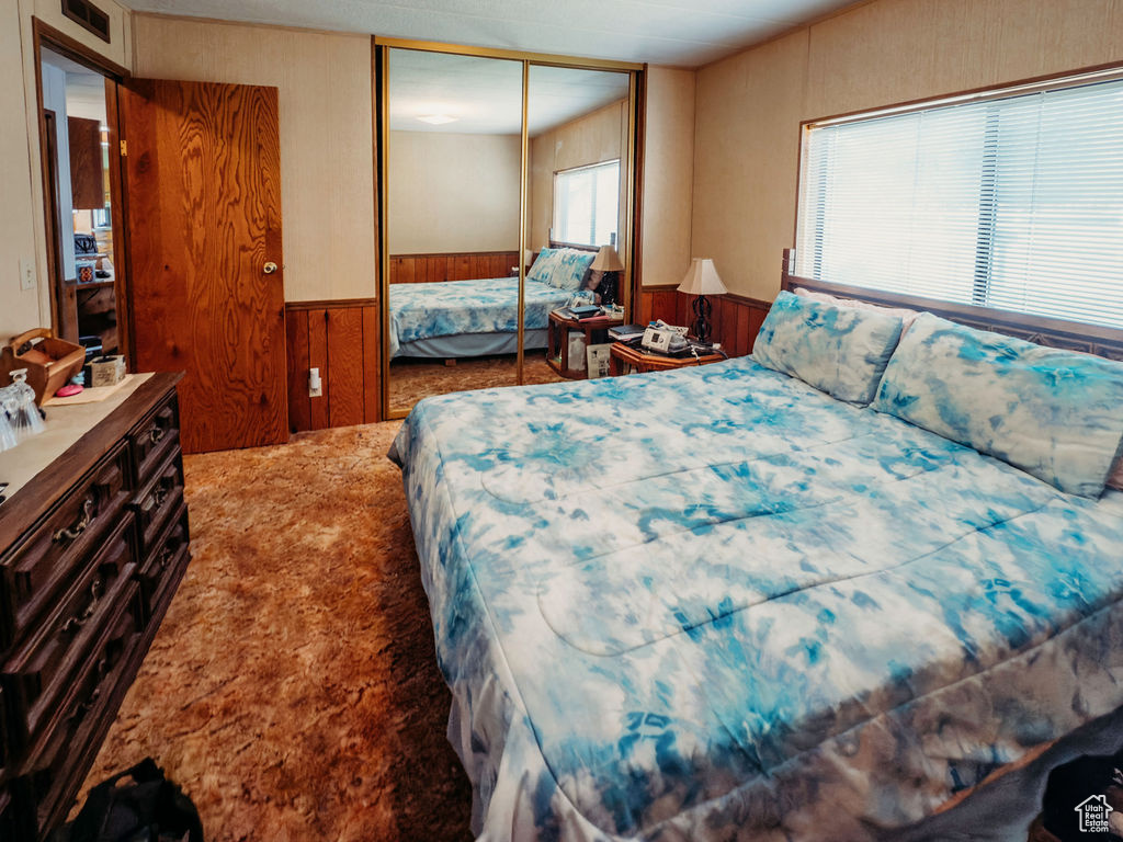 Carpeted bedroom featuring a wainscoted wall, wooden walls, and a closet