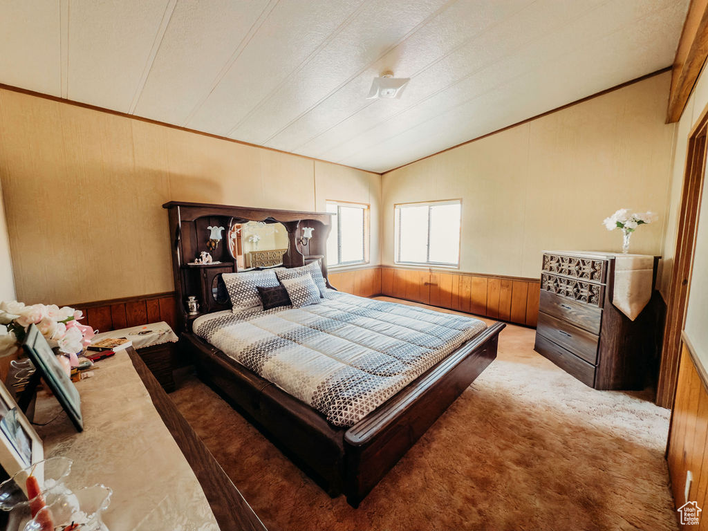 Bedroom with carpet floors, wood walls, lofted ceiling, crown molding, and wainscoting