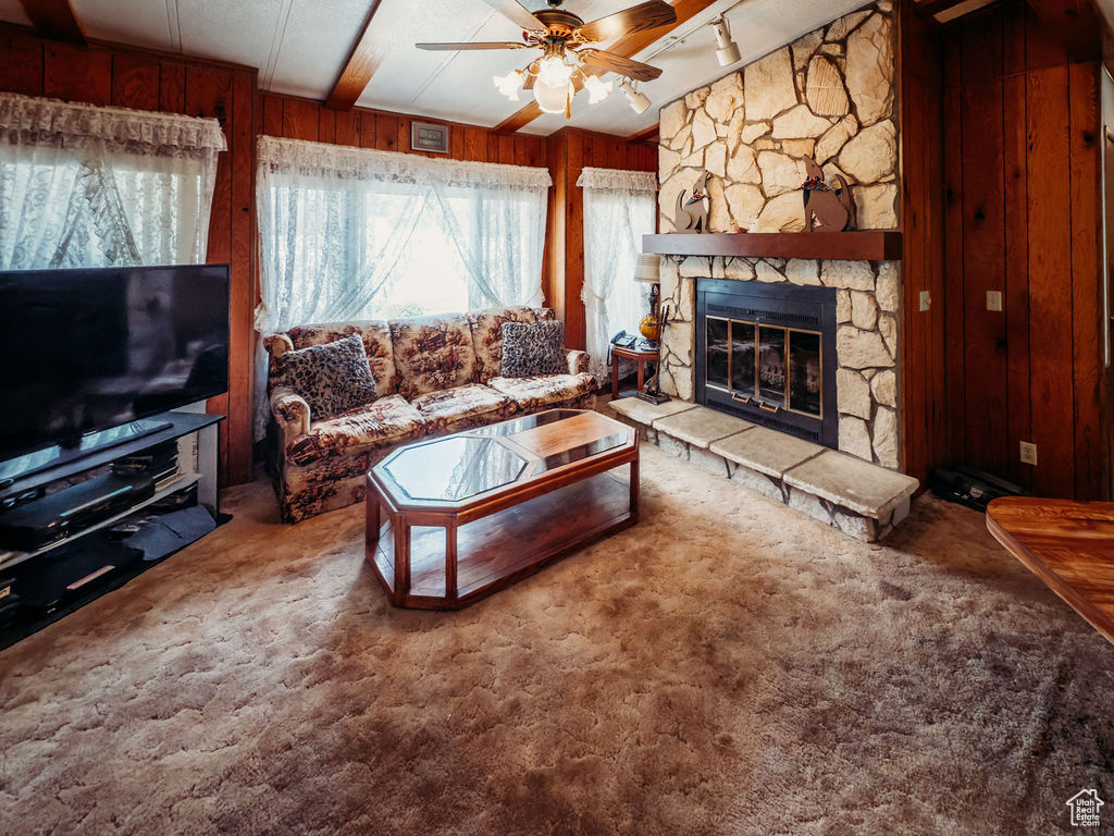Carpeted living room featuring wooden walls, a ceiling fan, a fireplace, and rail lighting