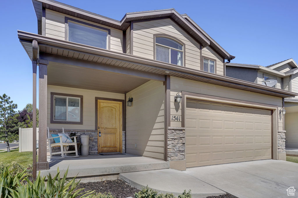 Townhome / multi-family property with stone siding, a porch, concrete driveway, and an attached garage