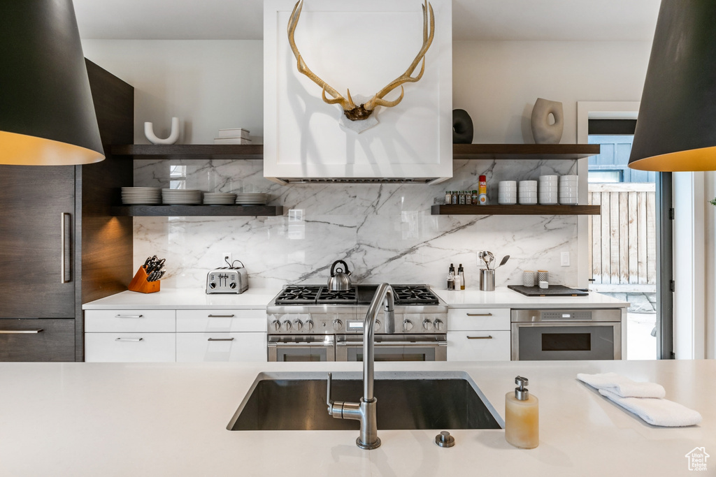 Kitchen with open shelves, high quality appliances, decorative backsplash, light countertops, and white cabinetry