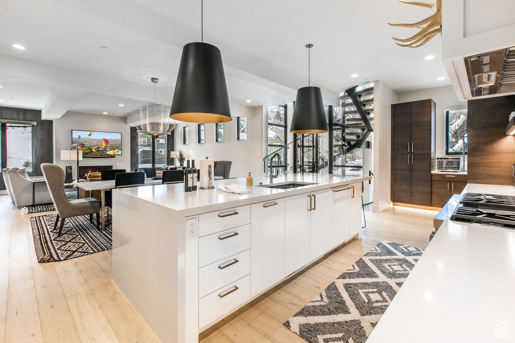 Kitchen featuring modern cabinets, white cabinets, light wood-style floors, hanging light fixtures, and light countertops