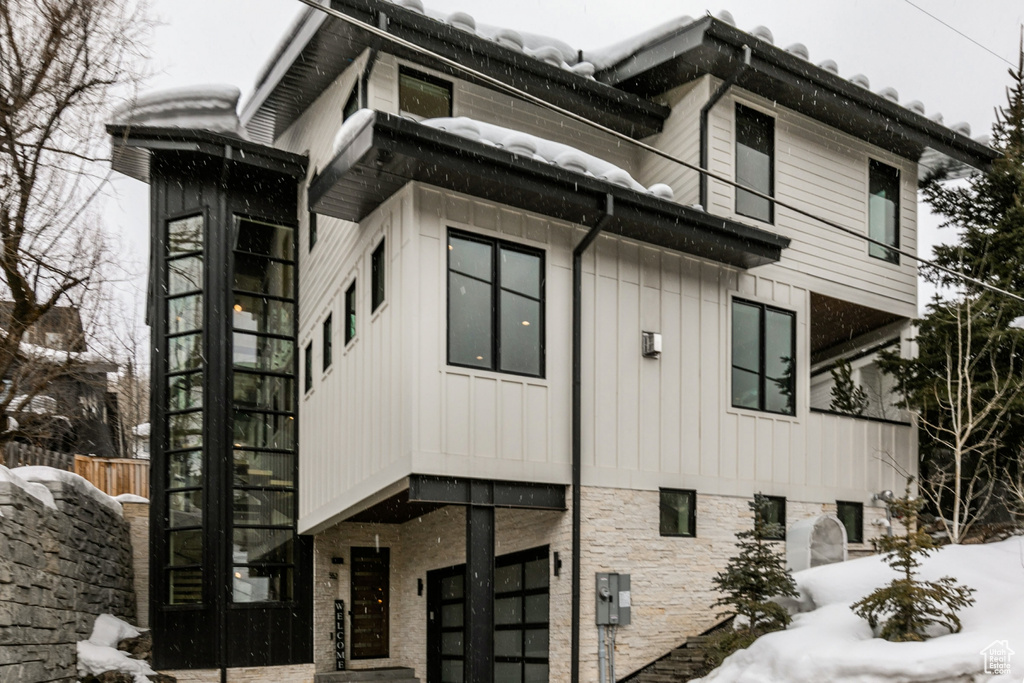 Snow covered property with a garage, board and batten siding, and stone siding
