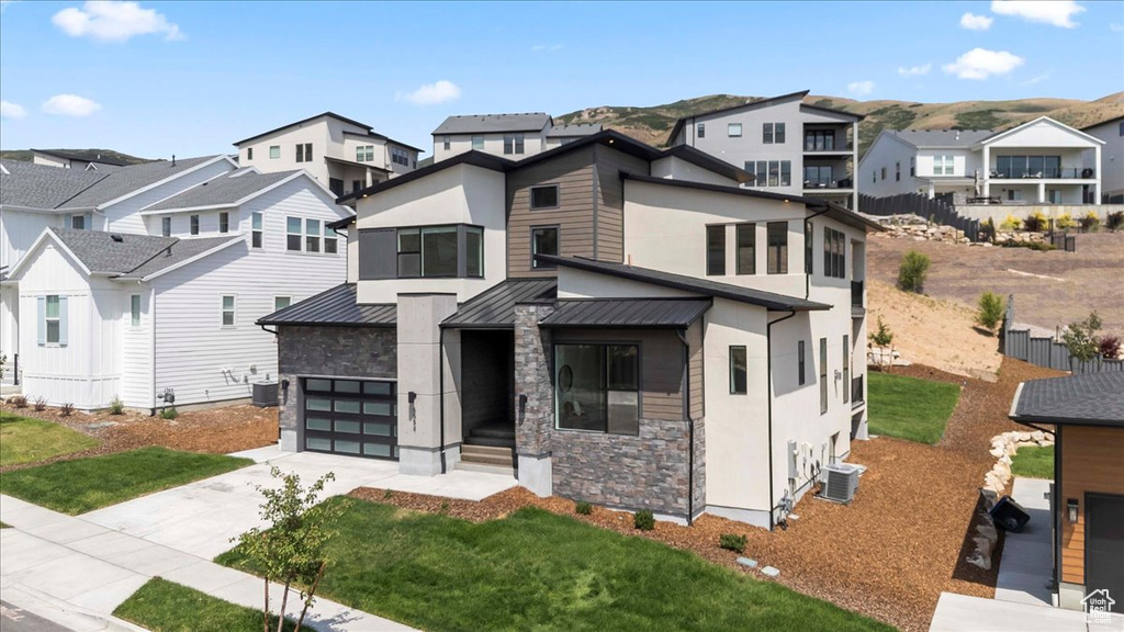 Contemporary home featuring a residential view, an attached garage, stone siding, concrete driveway, and a standing seam roof
