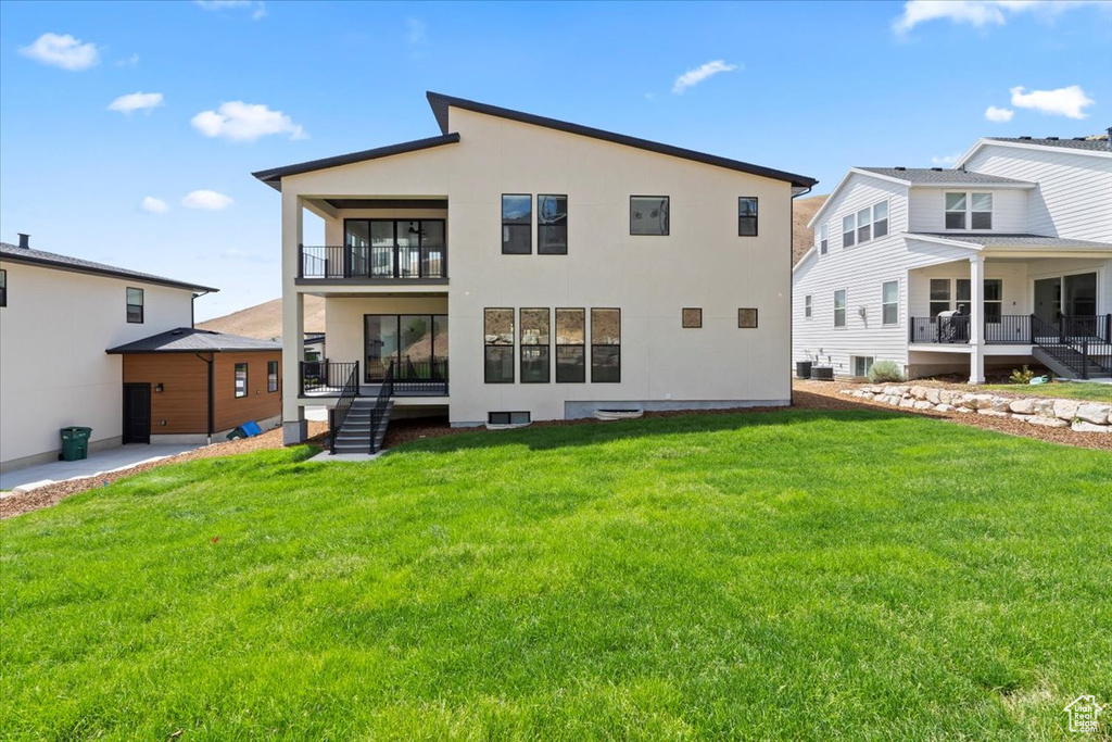 Rear view of house with a balcony, a lawn, and stucco siding