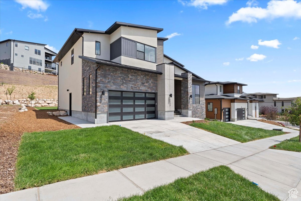 Contemporary house with stone siding, stucco siding, a garage, driveway, and a front lawn
